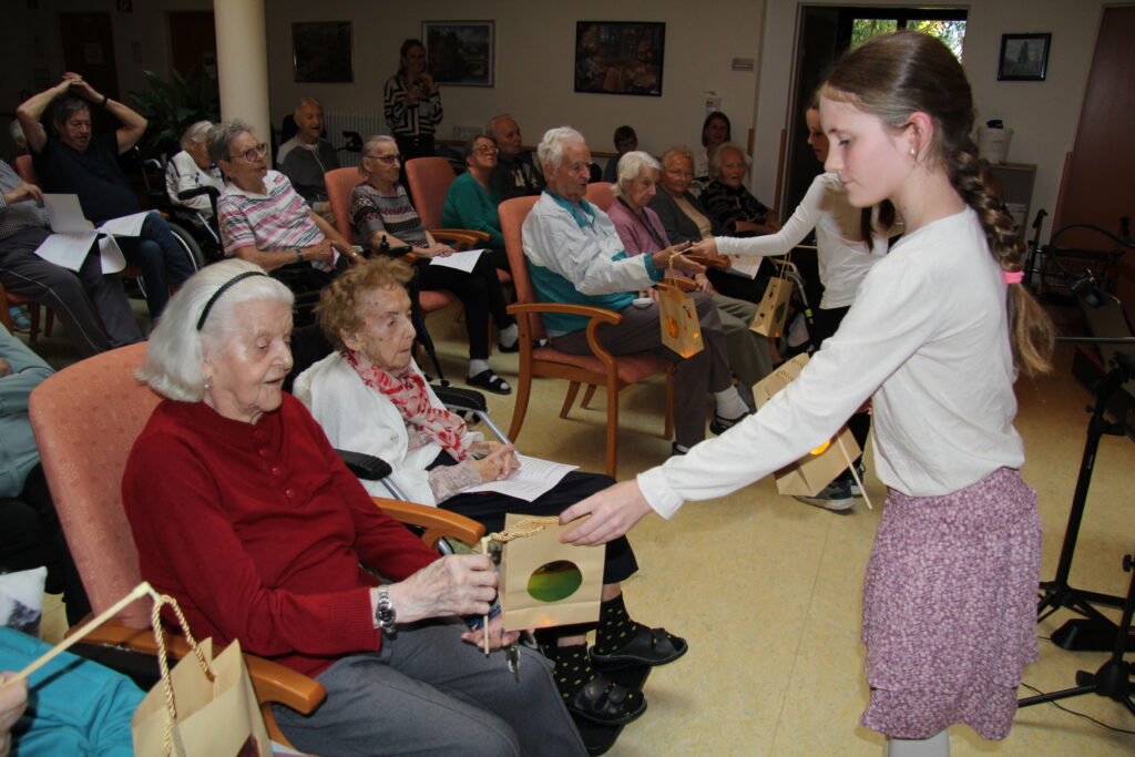 Kinder überreichen älteren Menschen in einem Pflegeheim liebevoll gestaltete Geschenkbeutel – intergenerationale Begegnung, Gemeinschaft, Seniorenbetreuung, soziale Teilhabe.