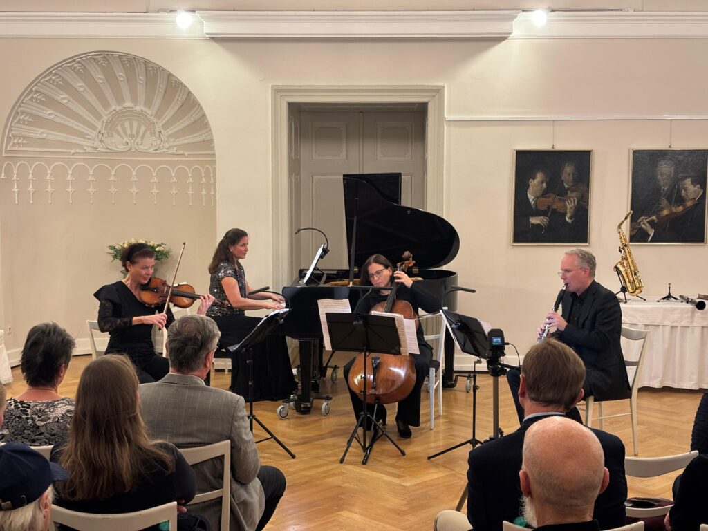 Live-Kammermusikaufführung im Festsaal des Thonetschlössls in Mödling mit vier Musiker:innen – Violine, Klavier, Cello und Klarinette – vor einem aufmerksamen Publikum in elegantem Ambiente mit klassischer Wanddekoration und Musikporträts.