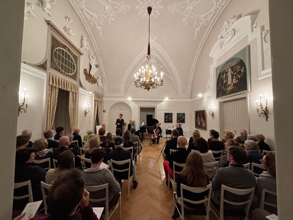 „Klassisches Konzert im Festsaal des Thonetschlössls in Mödling mit Cellistin, Pianistin und Sprecherin vor aufmerksamem Publikum in eleganter, historischer Kulisse.“